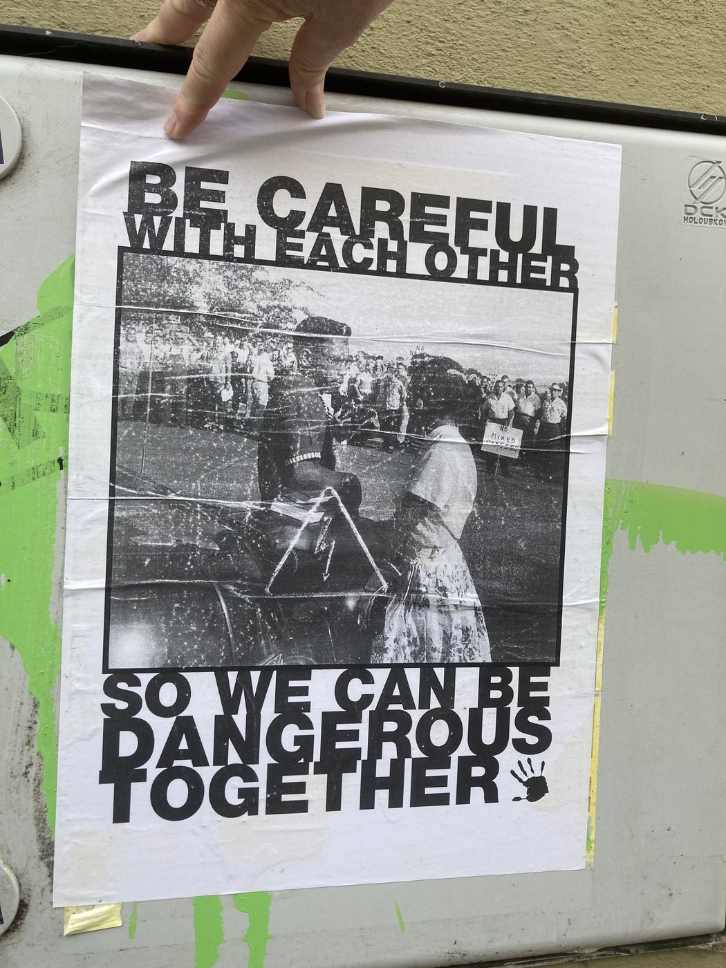 A hand holding a poster reading: be careful with each other, so we can be dangerous together